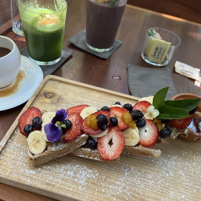 Waffles con frutos rojos, un jugo verde y un smoothie en una mesa del jardín de ARCANA