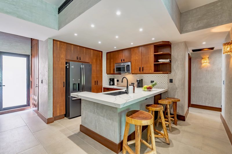 Kitchen with a white stone island and wood stools, a stainless steel refrigerator, wood cabinets and a patterned tile backsplash