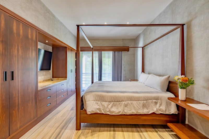 Bedroom with a four-post canopy bed, built-in wood wardrobes with a TV and a vase of flowers