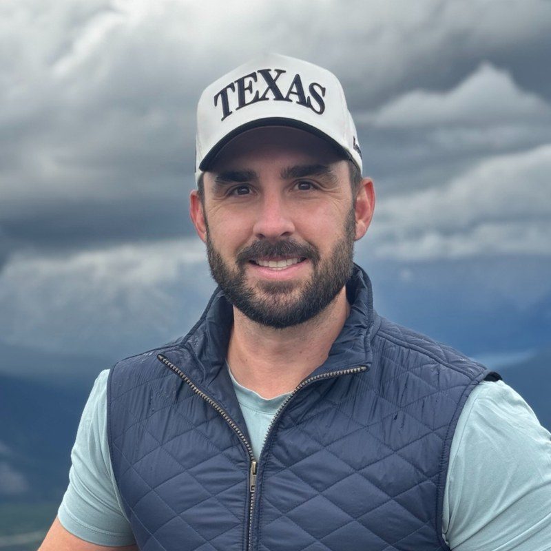 Isaac, owner of PH 315, smiling in a white Texas cap and a navy quilted vest under a cloudy sky