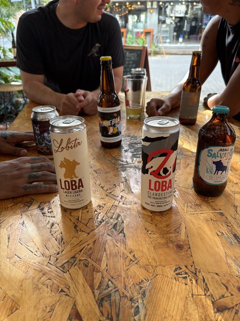 Latas y botellas de cerveza artesanal mexicana sobre una mesa de madera en CMC