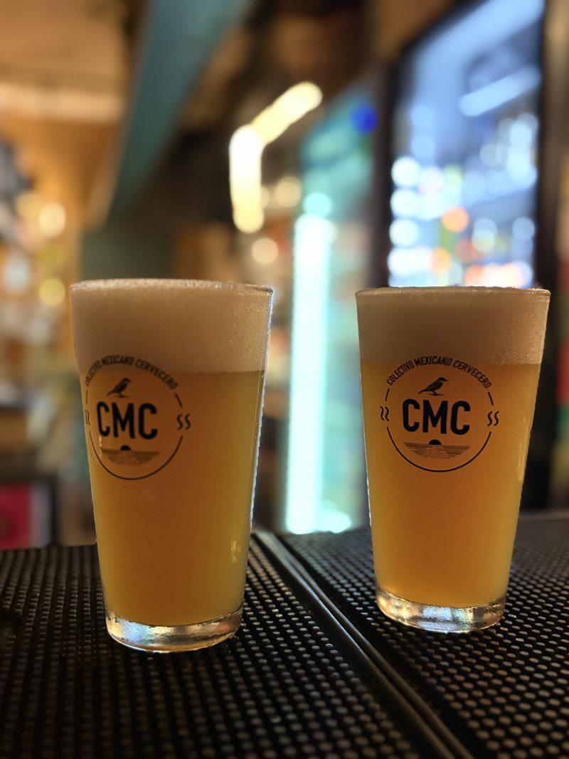 Dos vasos de cerveza turbia con el logotipo de CMC, sobre la barra