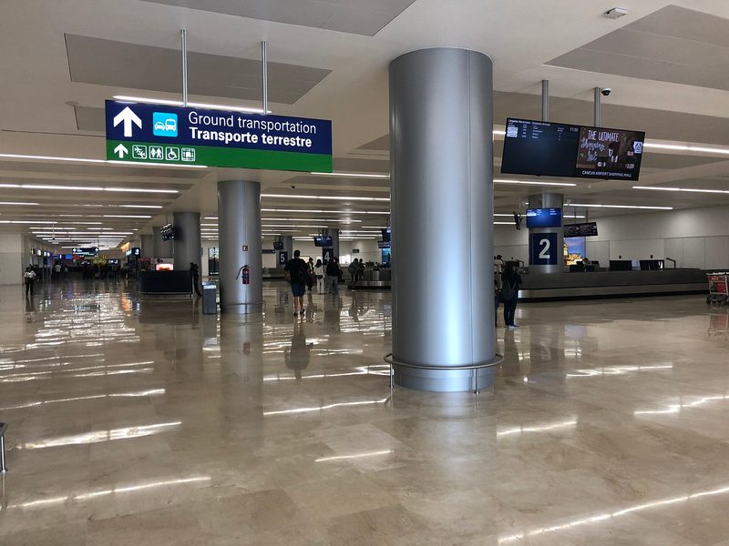 Arrivals hall at Cancún International Airport, with signs to ground transportation and baggage reclaim.